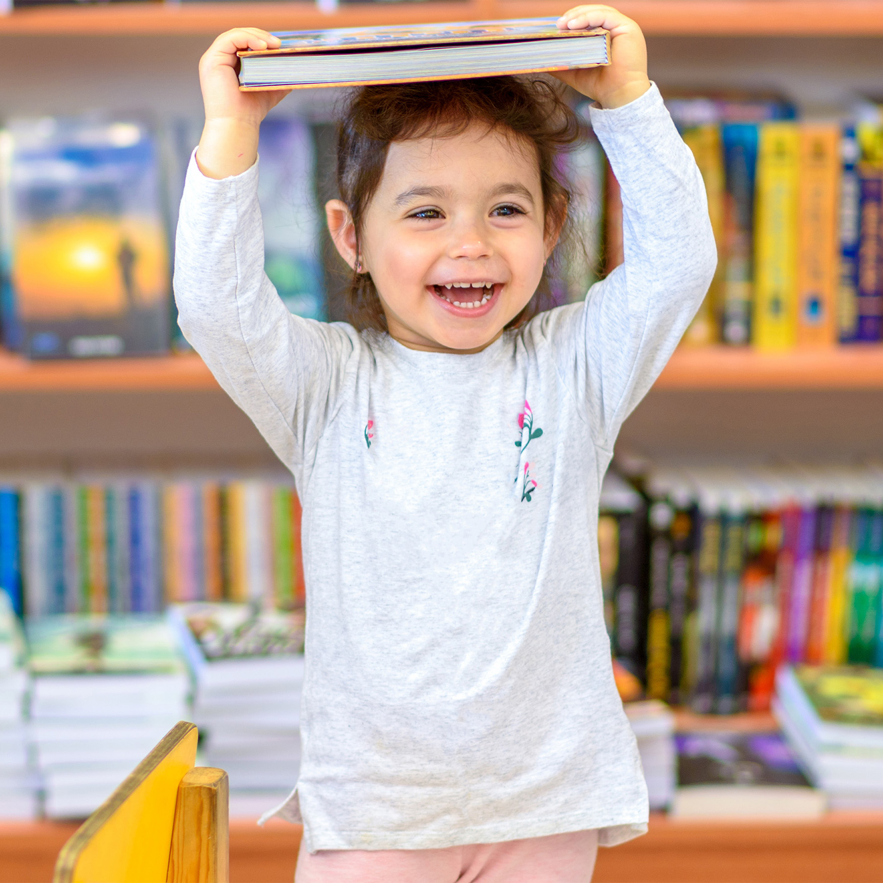 Toddler laughing and holding a book to her head.