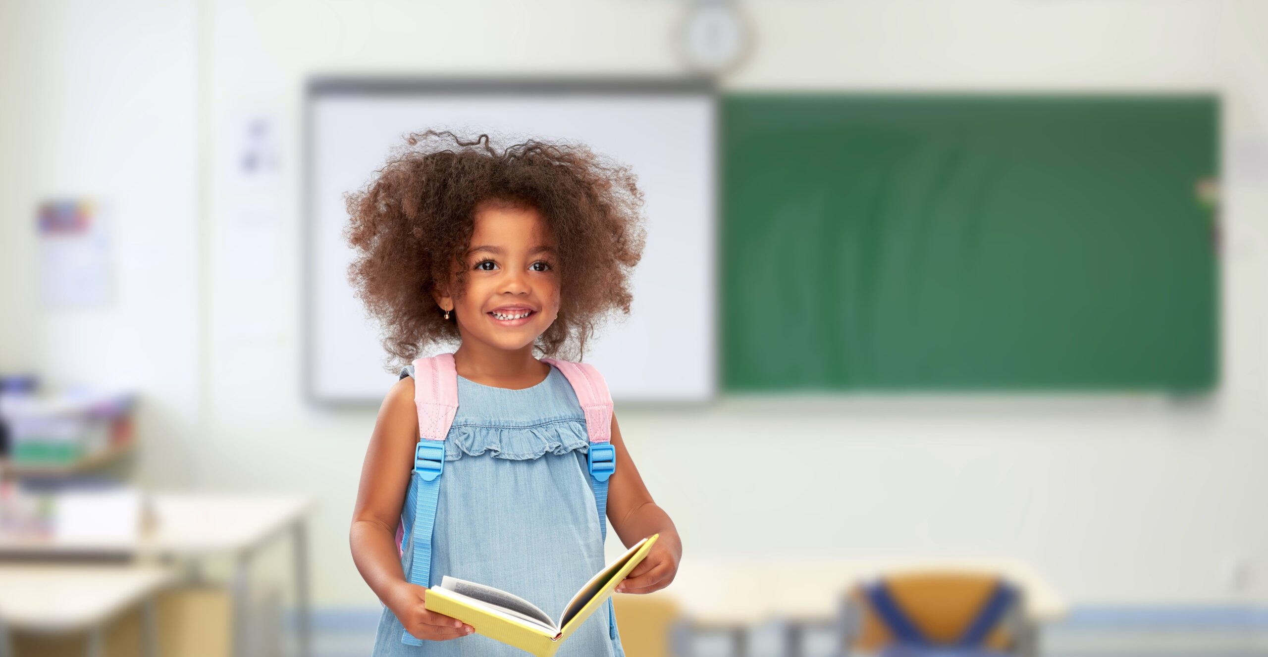 Happy little African girl with book and backpack.