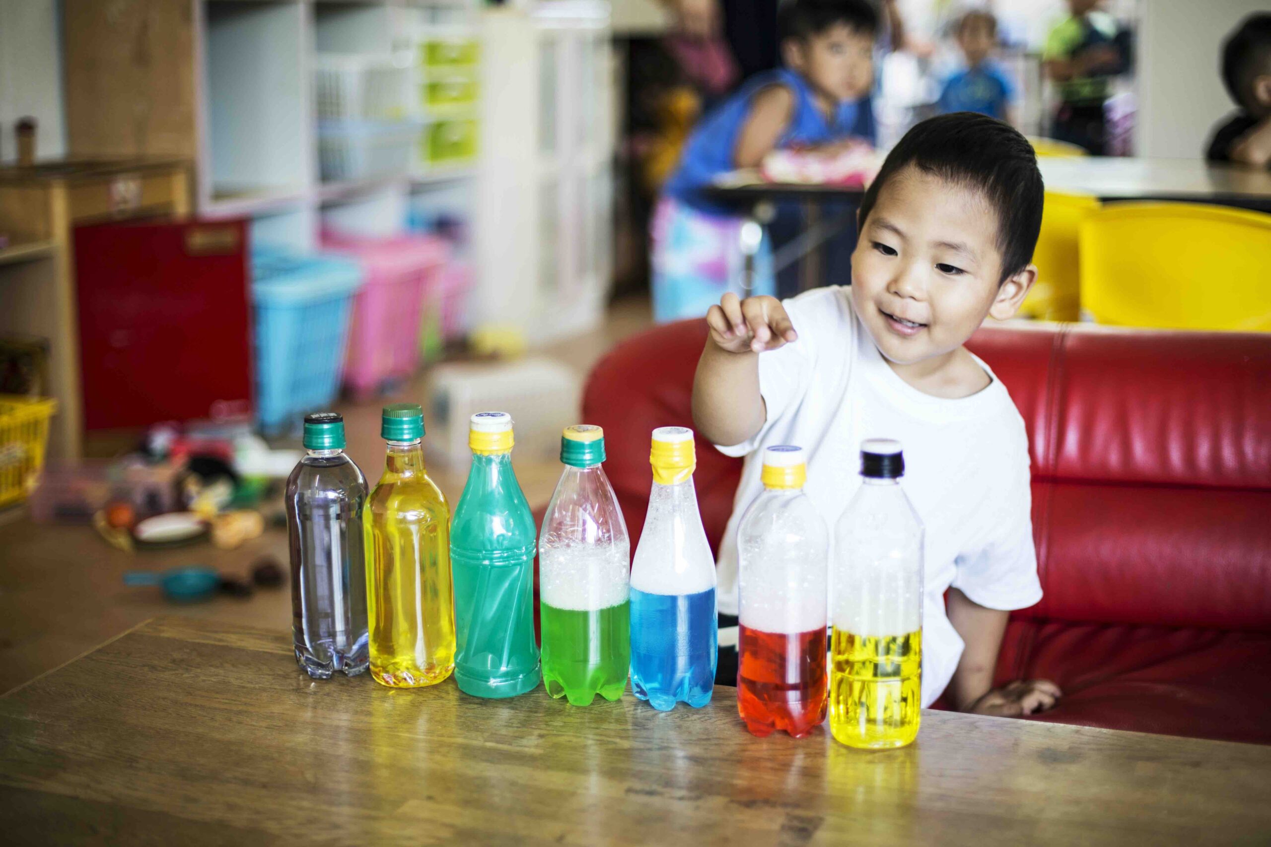 Young boy playing with a selection of bottles with colourful liquids in a preschool.